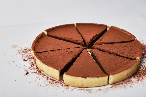 Dark chocolate tart cut up into slices against a white background