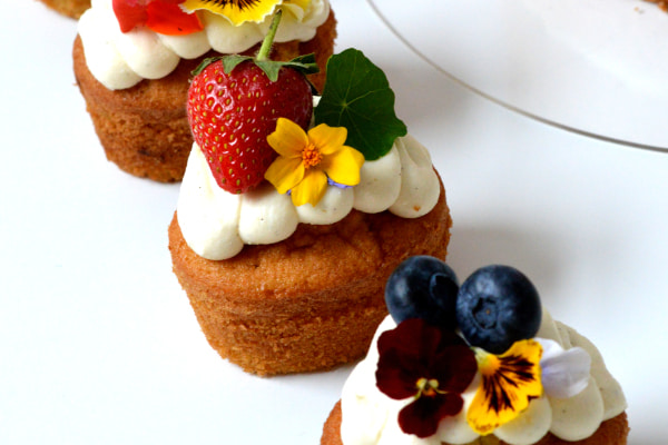 Three cupcakes decorated with frosting, fruits, and flowers