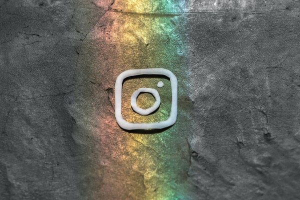 instagram icon on a slate background with rainbow colours shining onto it