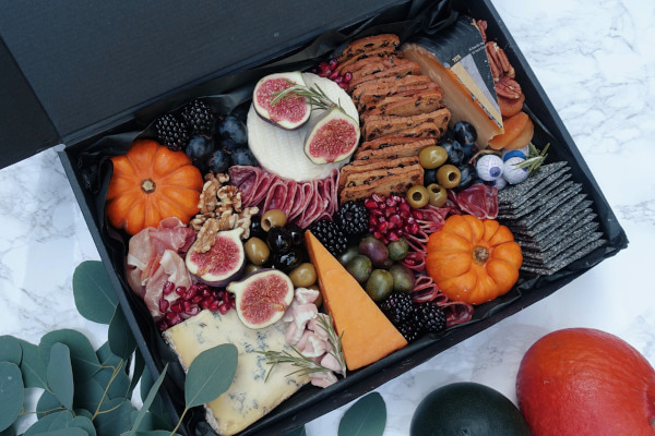 Box filled with cheese, crackers, cold meats, and pumpkins