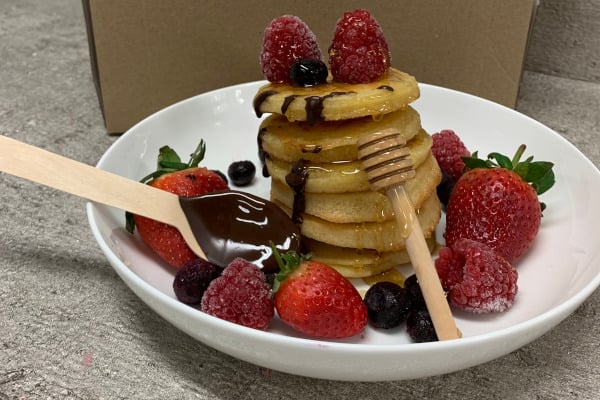 stack of pancakes topped with fruit, honey, and chocolate sauce