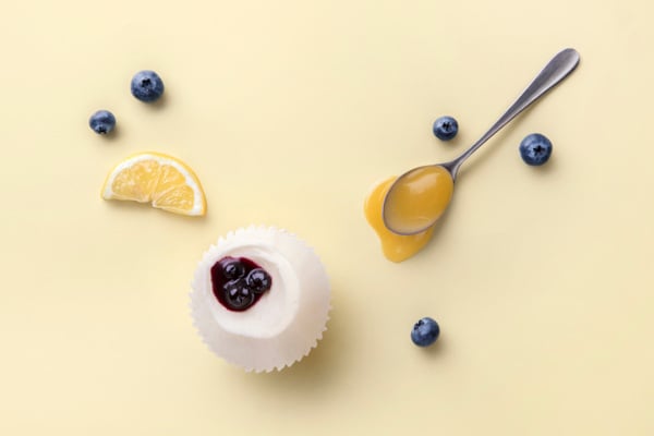 cupcake on a pale yellow surface with blueberries and slice of lemon