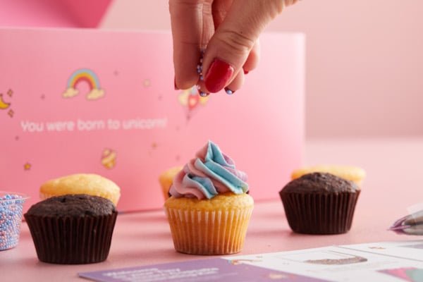 Hand sprinkling sprinkles onto unicorn cupcake