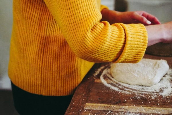 person in yellow jumper making pizza dough