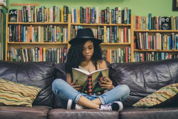 Girl reading cross-legged on the sofa, behind her are bookshelves full of books