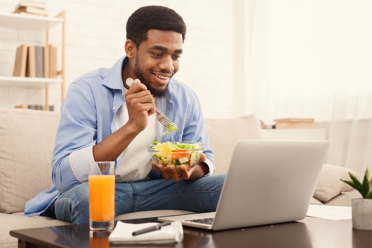 Person eating bowl of salad in front of laptop